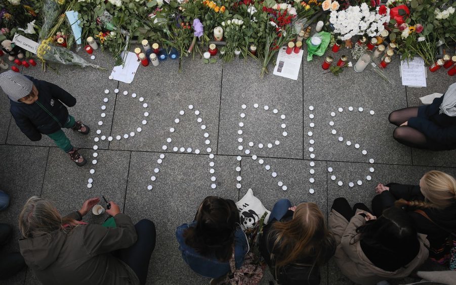 People finish arranging candles into the word "Paris" next to flowers and messages left at the gate of the French Embassy