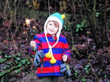 Little child in winter clothes holding burning sparkler