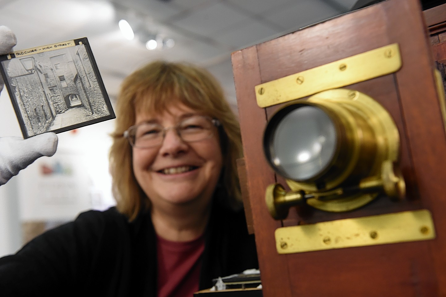 Liz Trevethick, museum officer with a magic lantern slide and projector at an exhibition in the Gallery at Elgin Library