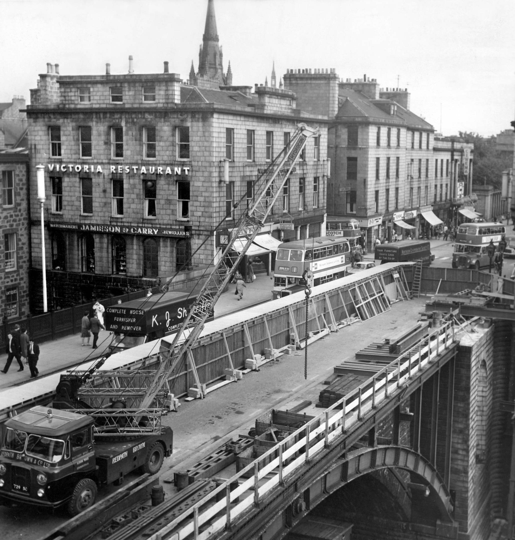 The Granite Mile The story of Aberdeen's Union Street p.76 by Diane Morgan A close up of the same view in 1963. The Victoria Restaurant, a popular rendezvous which opened in the mid-fifties, has replaced the Aberdeen Hotel. Jamieson & Carry, jewellers, is below, and in the foreground is a glimpse of the south side of Union Street before the shops went up. Right of the bus, just visible, emerging from Belmont Street (traffic on the bridge is single line, and buses have been re-routed) is the tall building which initially included the Archibald Simpson office. It was rebuilt after the fire of 1826, a "twin" has been added, and the group expanded to the east. This block now numbers Nos 122 1/2-132 and currently includes Symington's/Reed Employment and O'Brian's/McColls. Irene Adair Fashions and Munros Tourist Agency were located here in modern times. Opposite the bus, extreme right are, No 122 James Allan/Mothercare and the former Queens Cinema. Aberdeen Journals Ltd 12.9.1963
