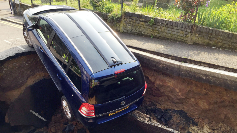 The parked car partially disappeared down the sinkhole