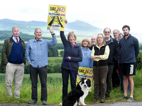 Bill and Carol Henderson hold up card to show relative height of pylons against Bennachie