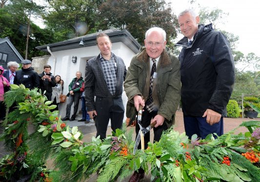 Official opening of National Trust for Scotland owned Inverewe House in the centre of Inverewe Gardens, Poolewe to the public.  Professor Ian Percy, former Deputy Chairman of the NTS uses garden shears to cut a garland to open the house. Also in the photograph are on the left Head Gardener Kevin Ball and on the right Simon Skinner, Chief Executive of the National Trust for Scotland. Pic by Sandy McCook