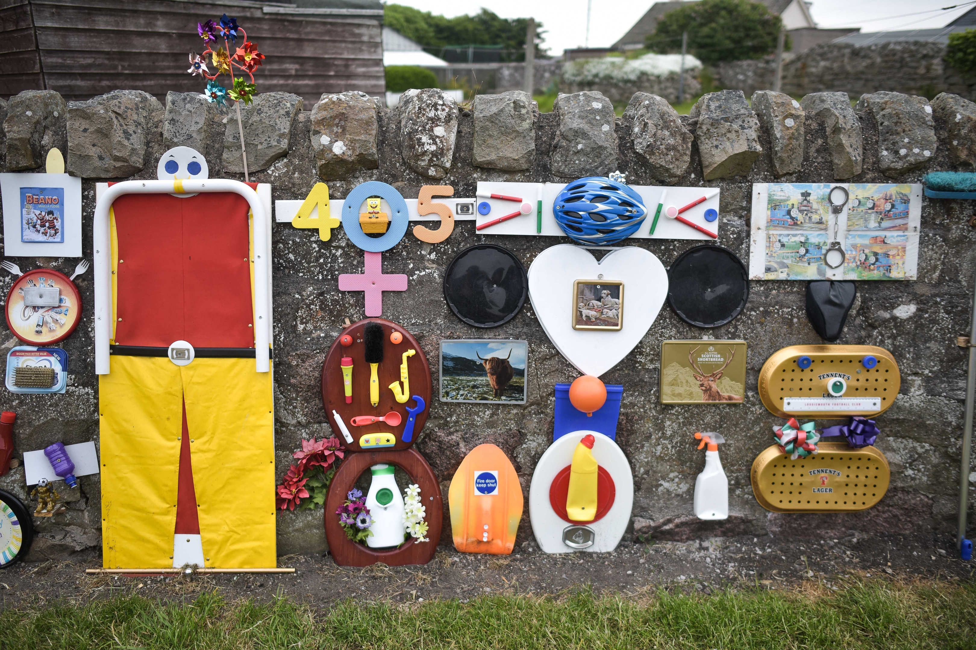 GV of the mural created by Charley Whyte, 76, on a wall in Lossiemouth, Moray on June 09 2016. Mr Whyte started the mural with just a chair in the corner as somewhere to sit during his evening walk. Since then he's added numerous other trinkets to the wall.  See Centre Press story CPLOO; A defiant retired plumber says he will not remove a bizarre mural he made from loo seats and toilet brushes. Charley Whyte, 76, started making the public artwork last August so that he could “brighten the place up”. And despite complaints from local residents, Charley said he won’t take down the mural in Lossiemouth, Moray. The mural, covered in random objects such as toilet brushes, loo seats and even Frisbees, stands at the entrance to Charley’s street. It is one of the first things drivers will see as they make their way into the town.