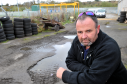 Iain Emslie, owner of A2B Cabs, beside his yard, in Chanonry Spur, Elgin, which he maintains should have been resurfaced following instatement of flood alleviation defences. Picture by Gordon Lennox.