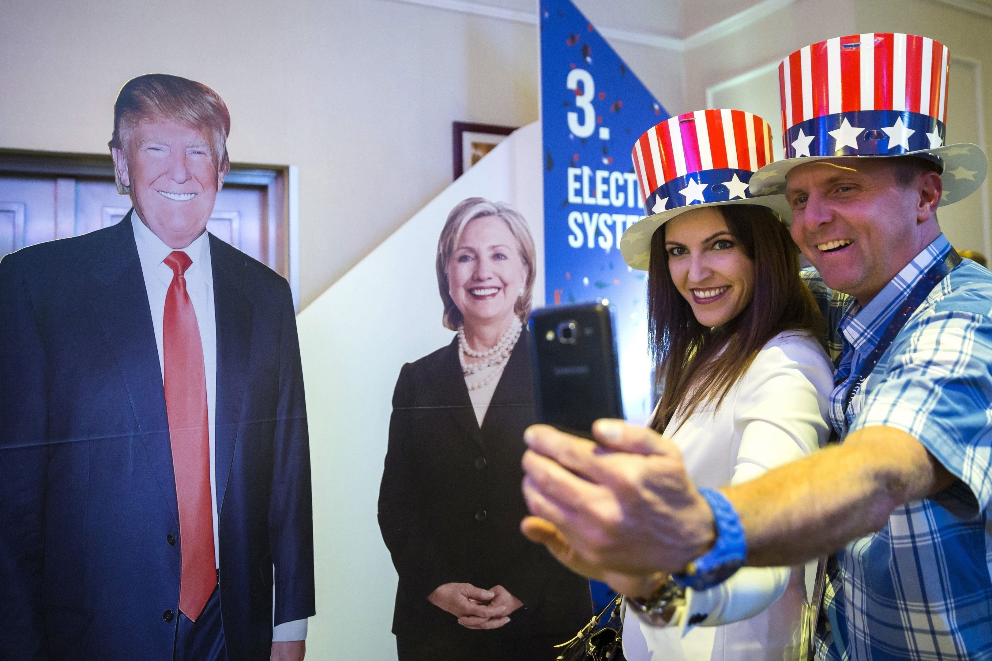 People in patriotic top hats take photographs next to cardboard figures depicting Donald Trump the Republican, left, and Hillary Clinton, the Democratic presidential candidates, during the Election Night Party at the US Embassy in Budapest, Hungary, Tuesday, Nov. 8, 2016. (Balazs Mohai/MTI via AP)