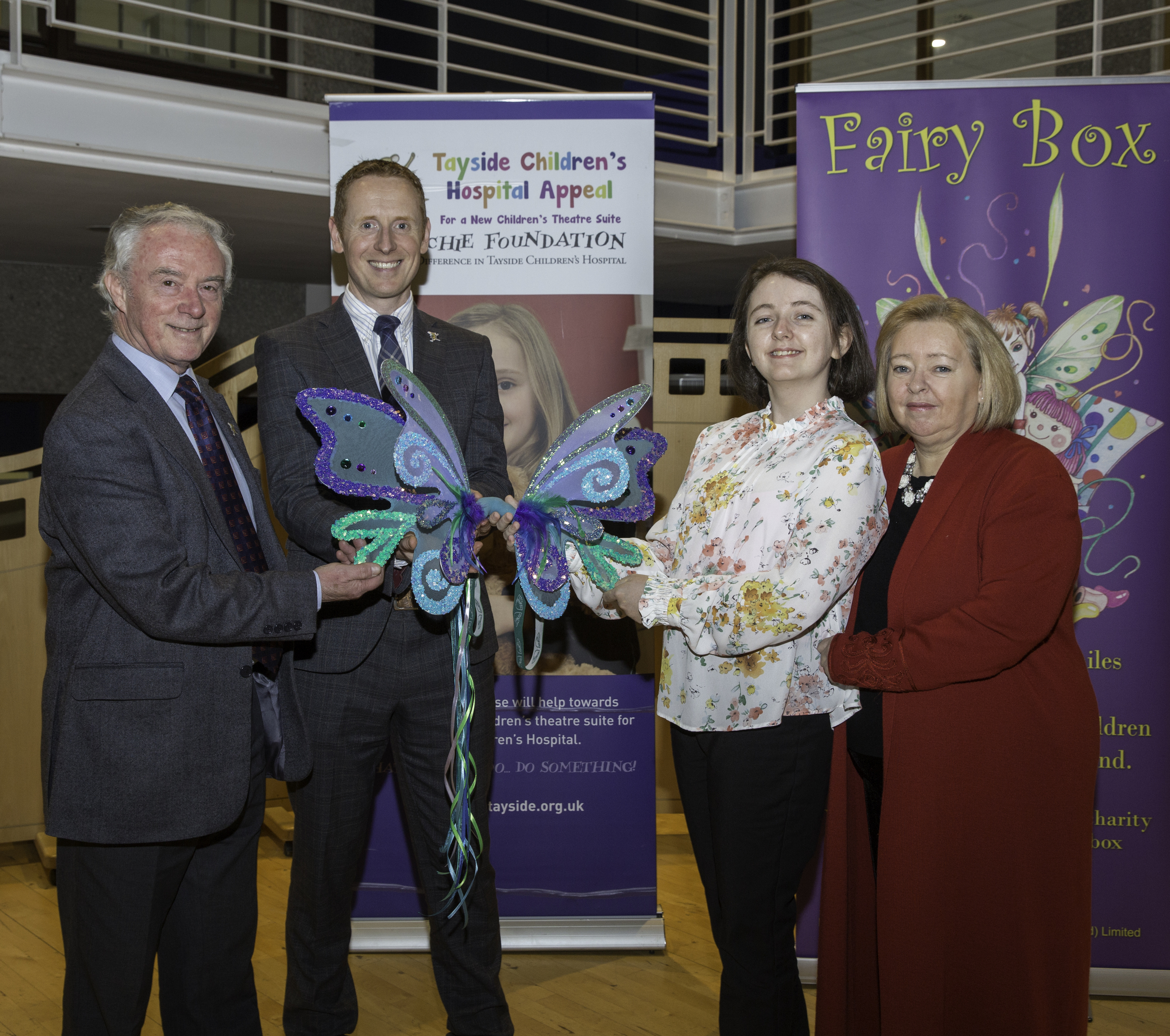 (L-R Joe Mackie, Chairman and David Cunningham, Chief Executive of The ARCHIE Foundation accept the Fairy wings from Aimee and Rosemary Butler)