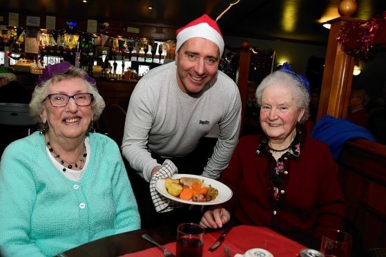 PETERHEAD FC MANAGER JIM MCINALLY SERVES UP THE TURKEY TO ELEANOR WALKER (L) AND DAISY DUNCAN AT THE BALMOOR CHRISTMAS LUNCH FOR LONELY PEOPLE.