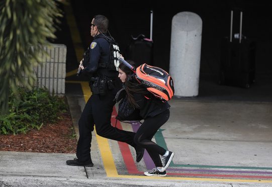 A young woman runs behind a police officer as they seek cover outside of Fort Lauderdale-Hollywood International airport