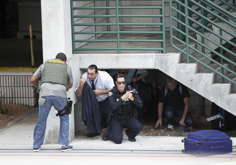 Law enforcement personnel shield civilians outside a garage area at Fort Lauderdale–Hollywood International Airport,