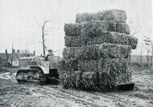 A Caterpillar Twenty crawler at work pulling a sledge full of bales of what might be pea haulm over some muddy ground.