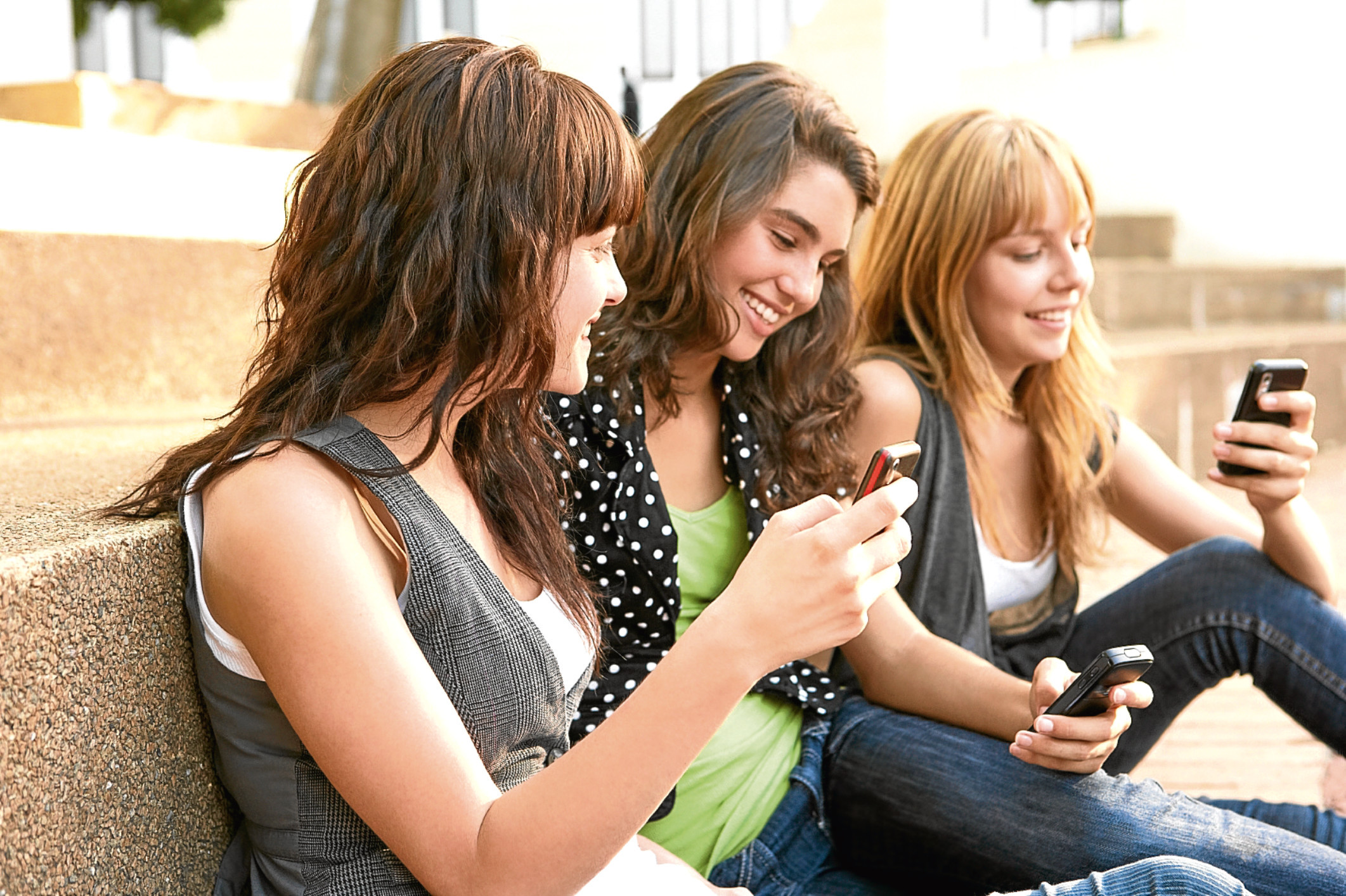 Group Of Teenage Students Sitting Outside On College Steps Using Mobile Phone