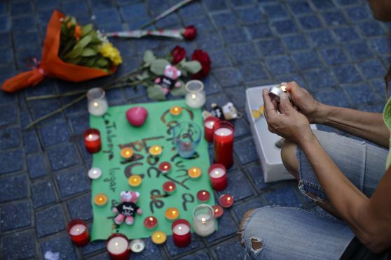 A woman lights a candle next to a paper that reads "Catalunya - place of peace" in Las Ramblas, Barcelona, Spain