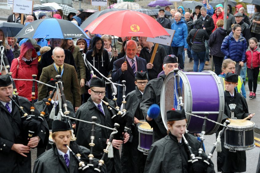 The massed choirs are led through Fort William by the Lochaber Pipe Band before performing on The Parade in the centre of the town