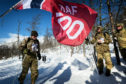 The RAF100 flag is waved at the finish line of the cross-country skiing race held on the final day of Ex-WINTERMARCH as one of the skiers crosses the line.