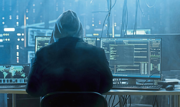 Dangerous Hooded Hacker Breaks into Government Data Servers and Infects Their System with a Virus. His Hideout Place has Dark Atmosphere, Multiple Displays, Cables Everywhere.