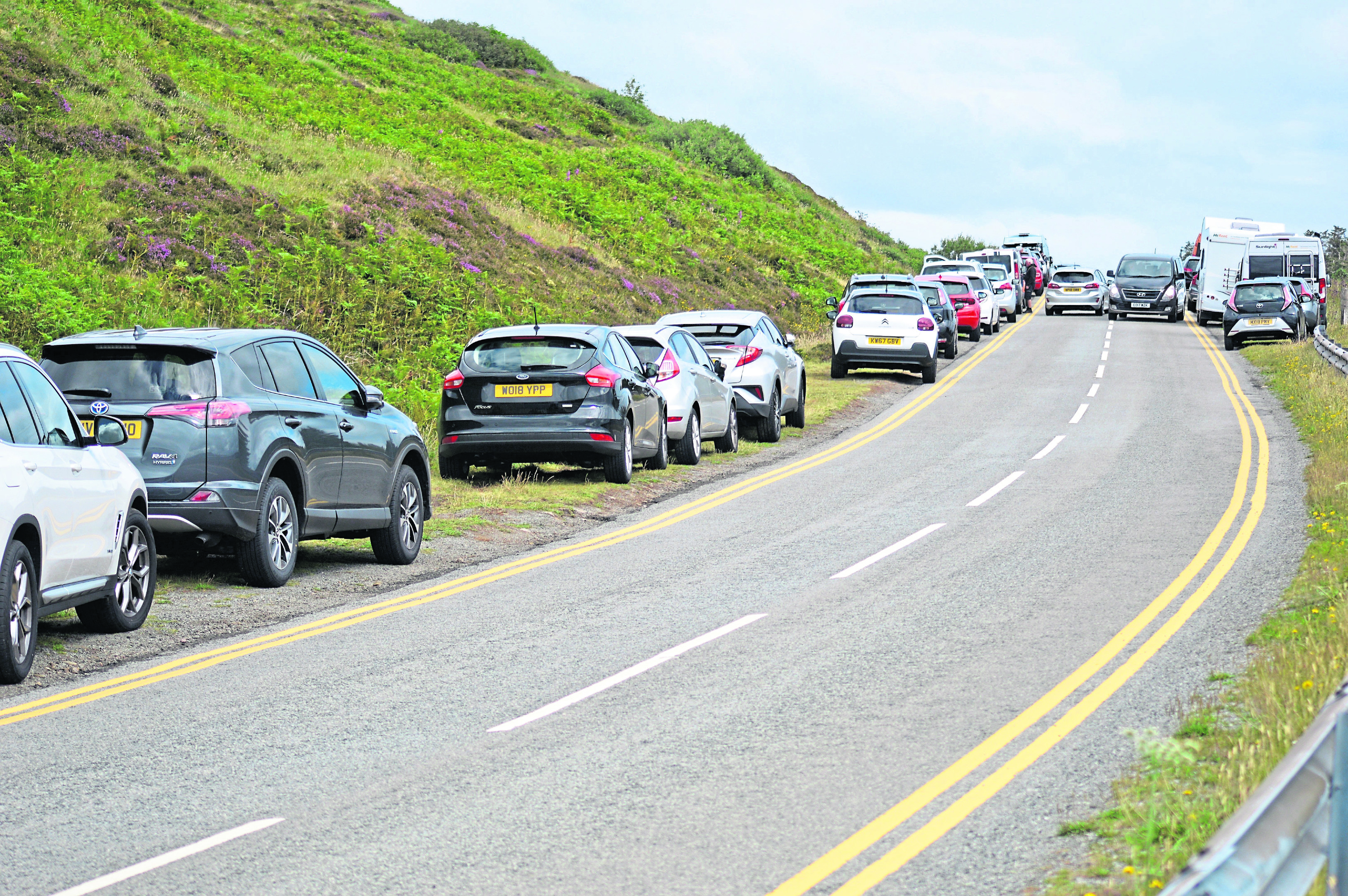 Tourist cars on the Isle of Skye fill up the side of the road as the nearby Old Man of Storr visitor car park is full.