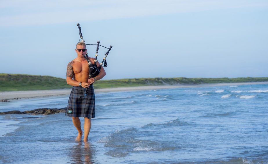 Skerryvore's piping maestro Martin Gillespie playing bag pipes in a kilt, walking in the sea