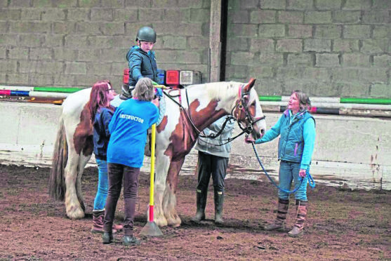 A young rider on Harry the horse along with three volunteers and an instructor.