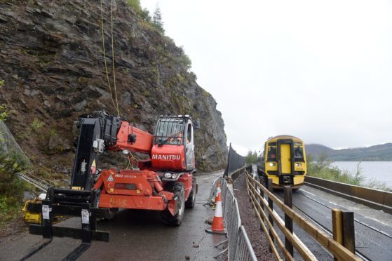 Engineers work high above the road last year as a train from Kyle passes works on the A890 Stromeferry bypass. Picture by Sandy McCook