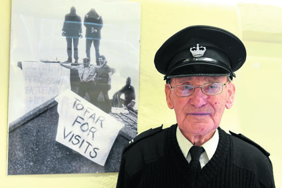 Jackie Stuart standing next to the picture of him being held hostage.