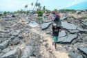 A man carries salvaged items as he makes his way through an area that was completely destroyed by an earthquake.