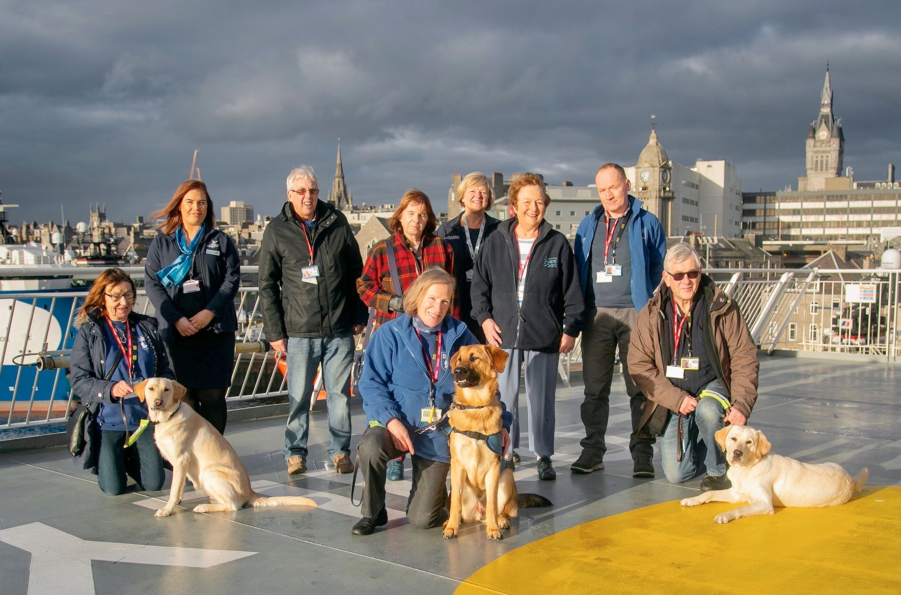 A group photo showing volunteers and their pups, staff from NorthLink Ferries and Puppy Training Supervisor Dave Mackay. 
Pups from left to right are Babs (yellow lab retriever cross aged 10 months), Storm (golden retriever cross German shepherd aged 9 months) and Faye (yellow lab retriever cross aged 10 months).