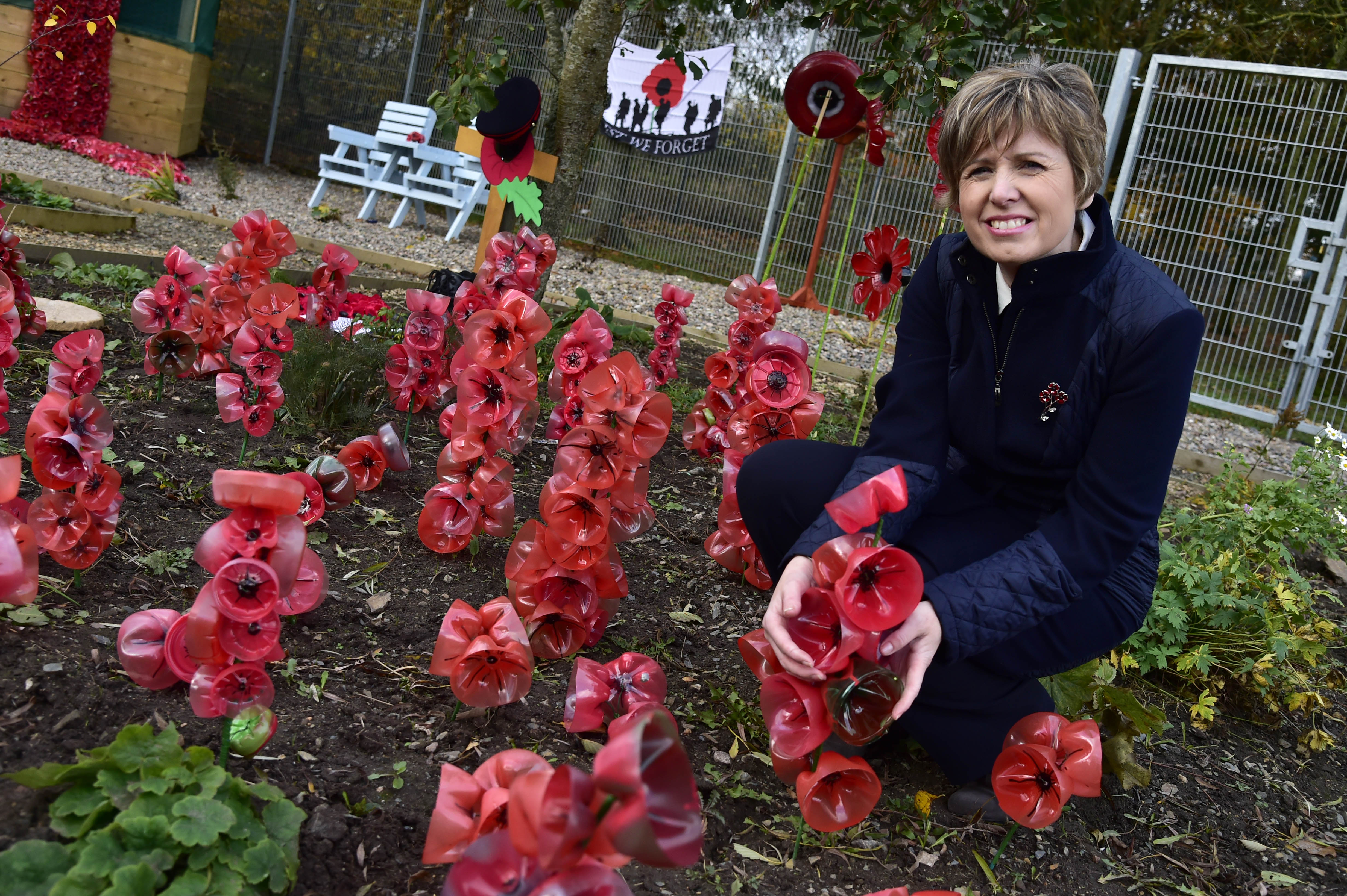 MINTLAW ACADEMY CLASSROOM ASSISTANT HEATHER REID IN THE THE THERAPEUTIC GARDEN BESIDE SOME OF THE POPPY DISPLAY SHE DESIGNED USING PLASTIC BOTTLES.