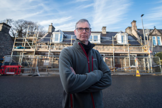 Phillip Murray on Rothes High Street in Rothes, Moray with his parents house covered in Scaffolding behind him.