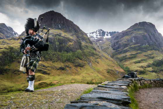 Traditional bagpiper in the scottish highlands by Glencoe