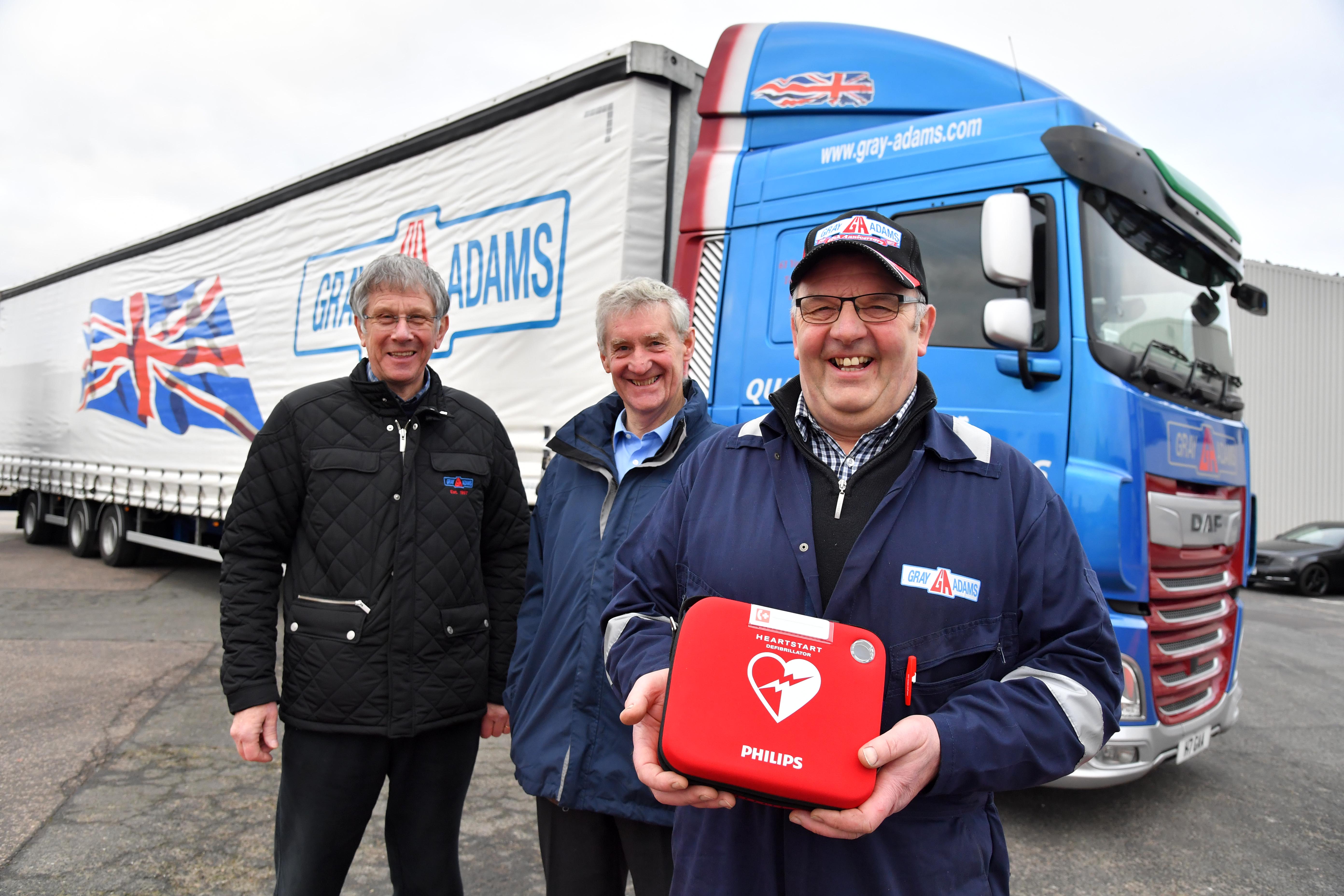 Murray Littlejohn of Gray and Adams shows one of the defibrillators which is being supplied to the company’s tractor units watched by joint managing director James Gray (L) and MSP Peter Chapman