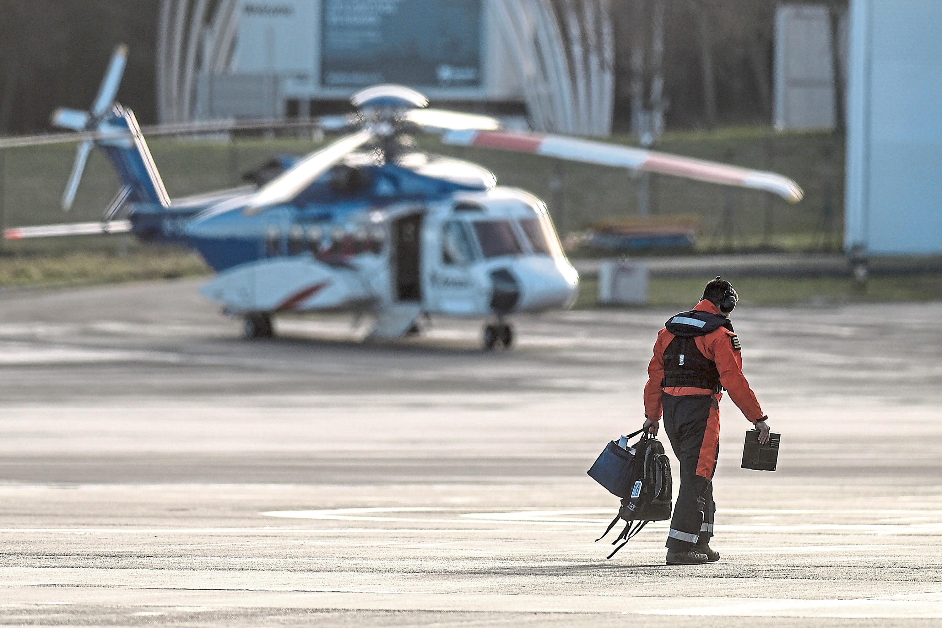 A pilot walks in front of a Bristow offshore helicopter at their base at Aberdeen Airport