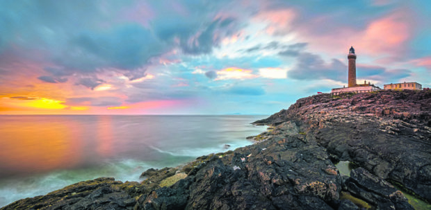 Lighthouse on cliffs of Ardnamurchan Point in colorful sunset,
