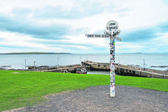 Signpost in John O'Groats with North Sea and Orkney islands in the foreground.