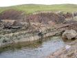 A field photo take at Stoer showing the laminar beds of sandstone in the bottom of the picture. In the middle is the impact deposit (12m thick at this location) that contains "rafts" of deformed pink sandstone.