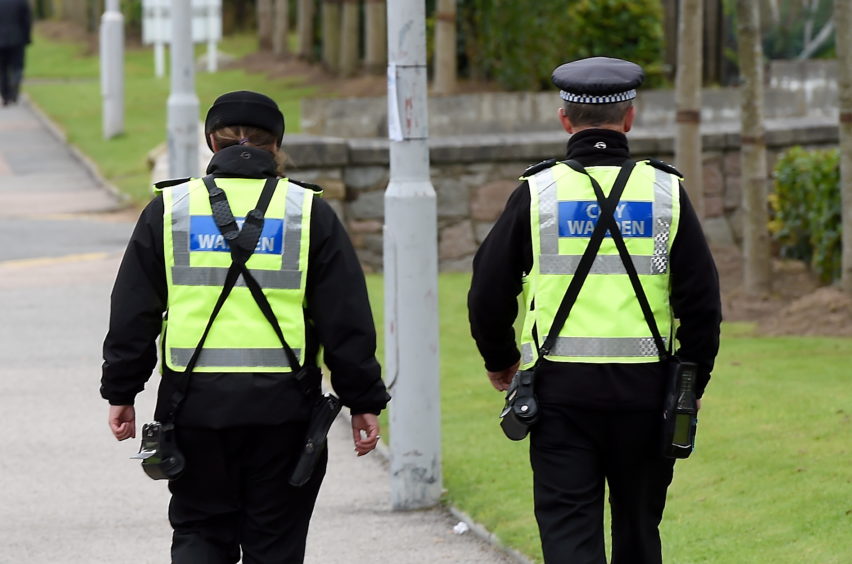 Two Aberdeen city wardens in uniform and high viz vests walk along a street.