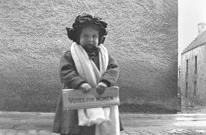 A small child holds a newspaper with Votes for Women on the front in Orkney Image: DCT
