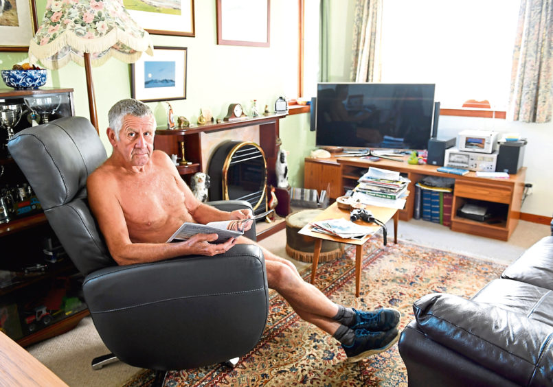 Robbie Gauld sitting in an armchair in his home reading a magazine wearing only socks and shoes.
