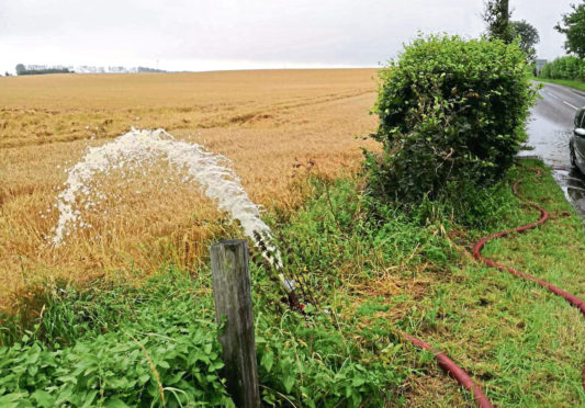 Water being pumped from a flooded house into a field of spring barley.