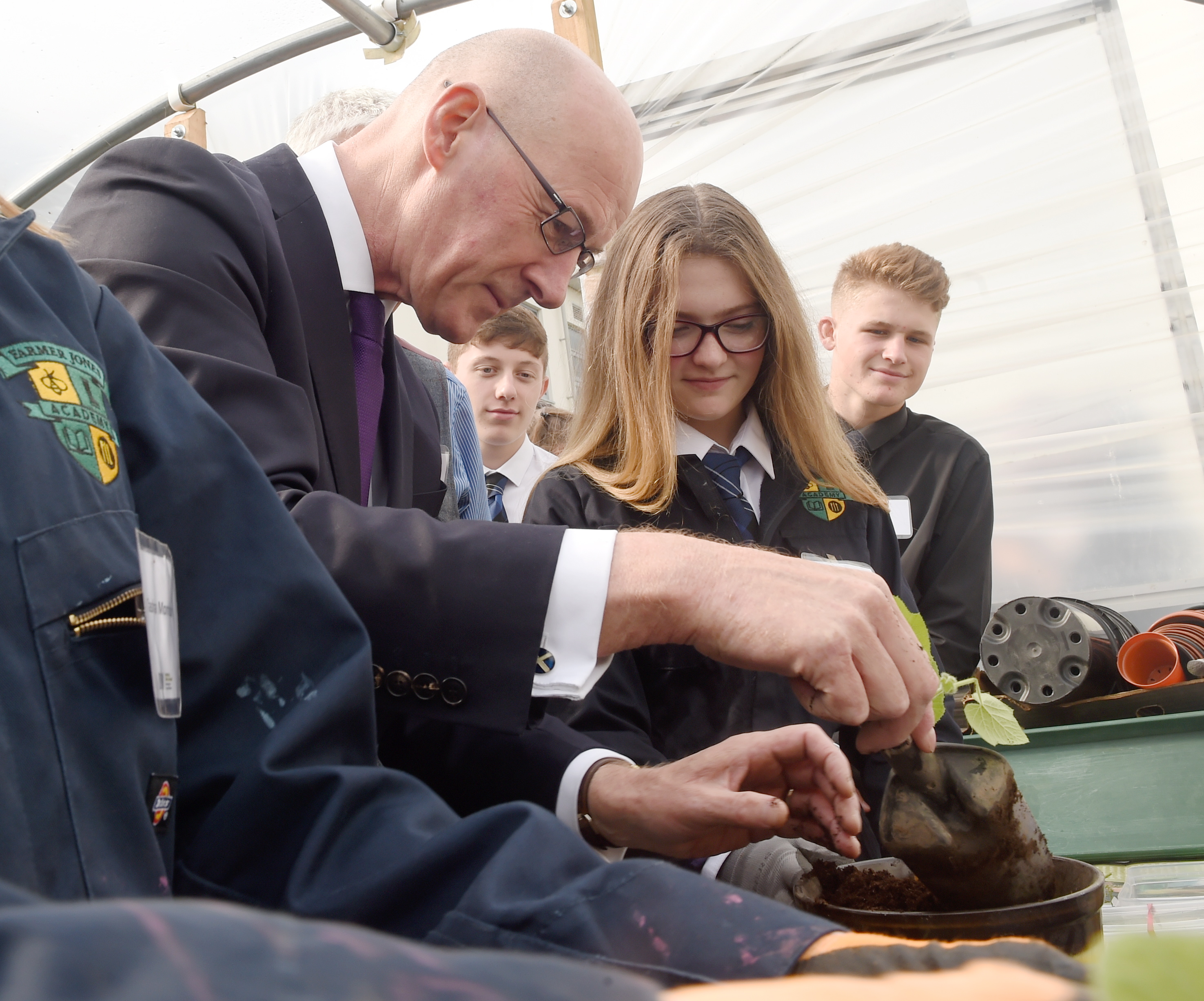 Deputy First Minister John Swinney yesterday visited Nairn Academy and the Farmer Jones Academy for pupils at the school. John Swinney, helped by pupils, plants a pumpkin the polytunnel. Picture by Sandy McCook