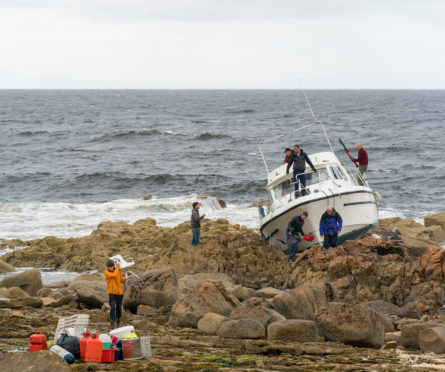 Coastguard, boat owners and friends salvage equipment before the boat breaks up on the rocks
