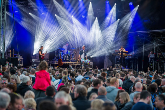 The stage set up with bright lights in the Northern Meeting Park. A huge crowd stands in front of the stage.