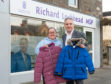 MSP Richard Lochhead and Debi Weir Founder of Moray School holding up free school uniforms and jackets they give away.