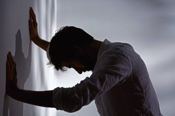 Man leaning with hands against wall, dark room