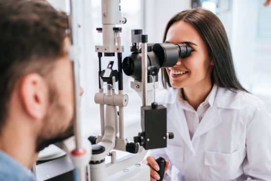 Attractive female doctor  ophthalmologist is checking the eye vision of handsome young man in modern clinic. Doctor and patient in ophthalmology clinic.