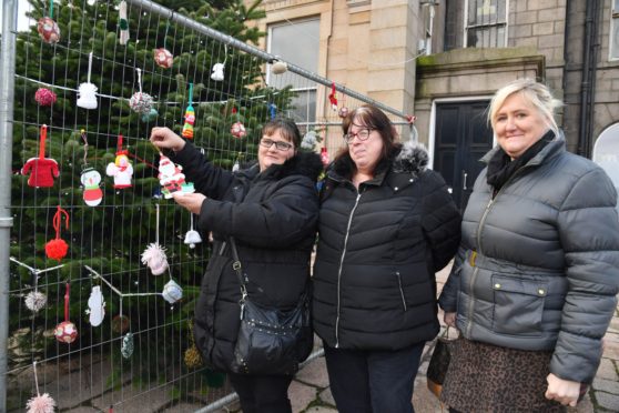ISOBEL ARTHUR-ROBERTSON PUTS UP A HAND KNITTED DECORATION ON THE PETERHEAD CHRISTMAS TREE WATCHED BY FELLOW MEMBERS OF THE PETERHEAD SOCIAL KNITWORK ALISON MACLEAN,   AND FIONA BUCHAN