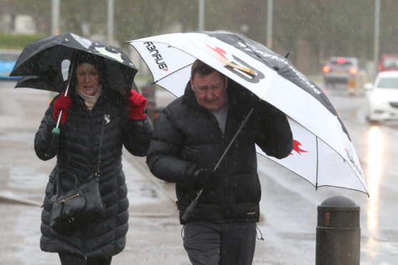 Inverness, UK, 9 February 2020. Two people walk in heavy rain and strong winds on the A96 in Nairn. Credit: Andrew Smith