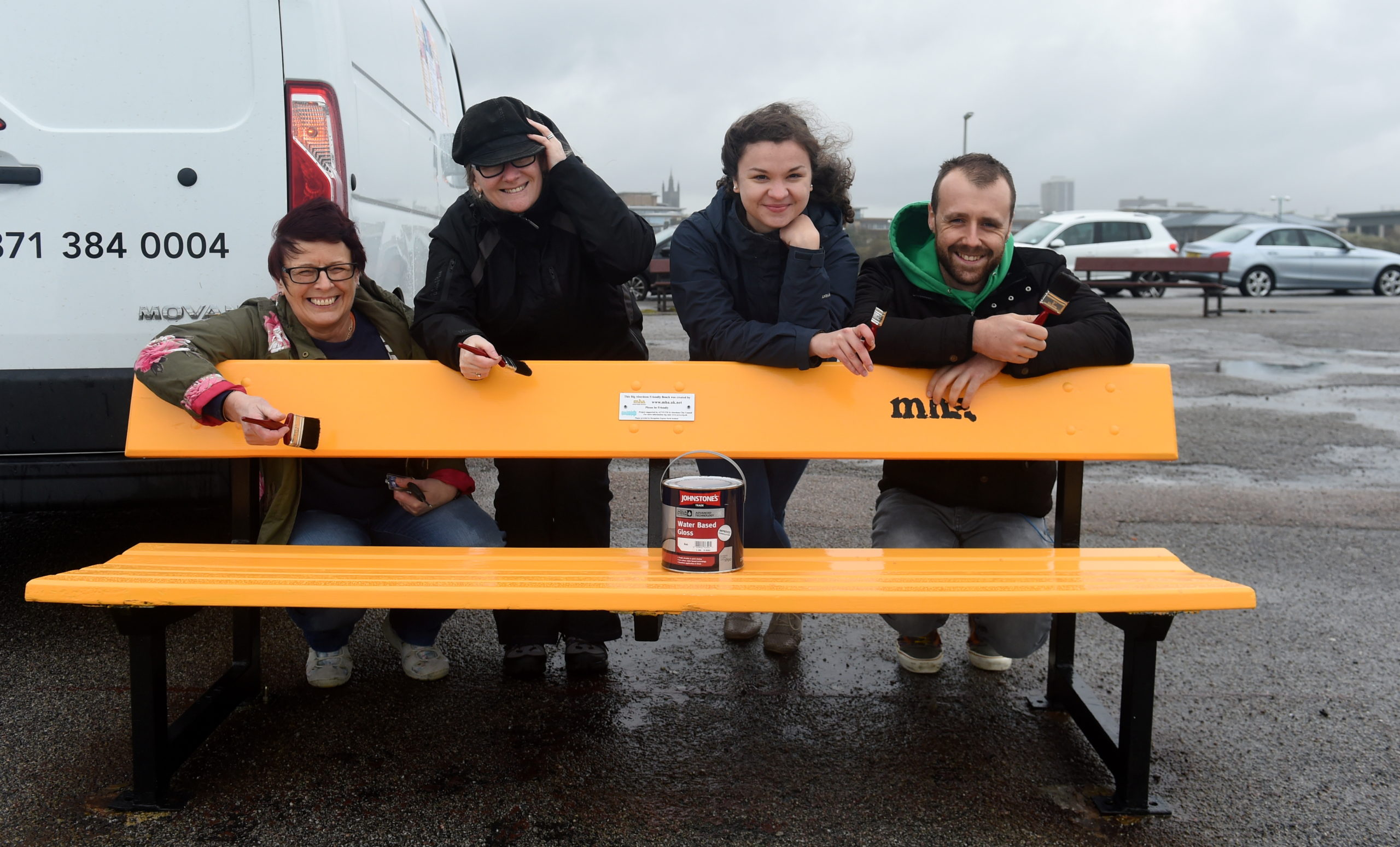 Four people painting a bench yellow with "MHA." written on it