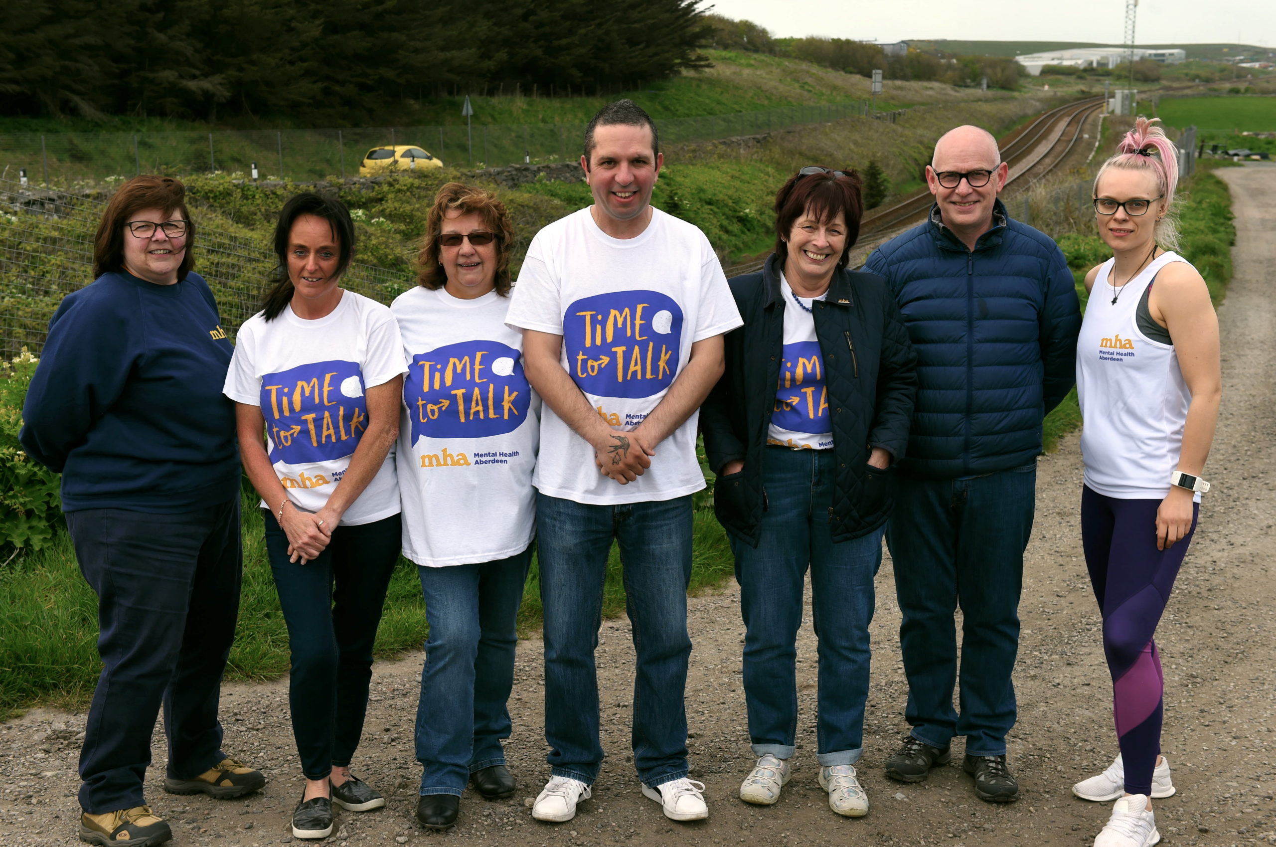 Mental Health Aberdeen staff stand in a line next to train tracks with MHA tshirts on