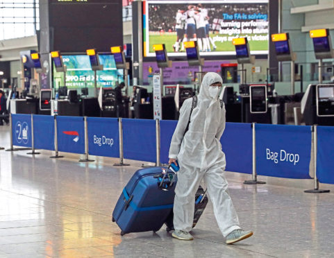 A passenger wearing protective clothing checks in for a flight from Heathrow Airport's Terminal 5 in London. PA Photo. Picture date: Thursday March 19, 2020. See PA story HEALTH Coronavirus. Photo credit should read: Steve Parsons/PA Wire